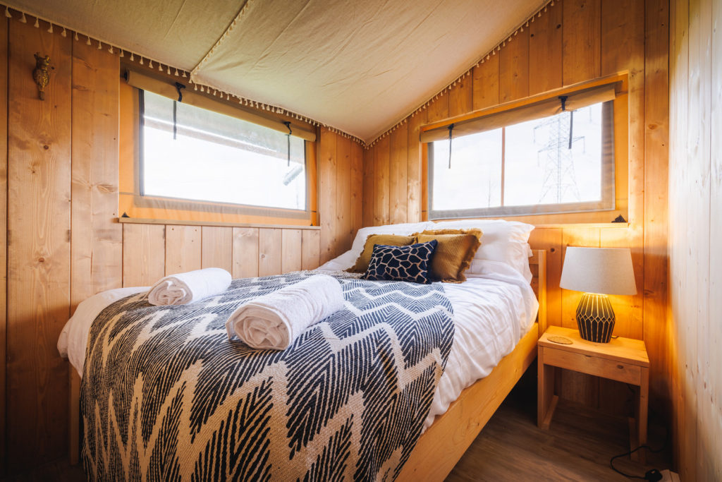 Photo of master bedroom in safari tent including draped ceiling, giraffe print cushion and African-styled lamp.